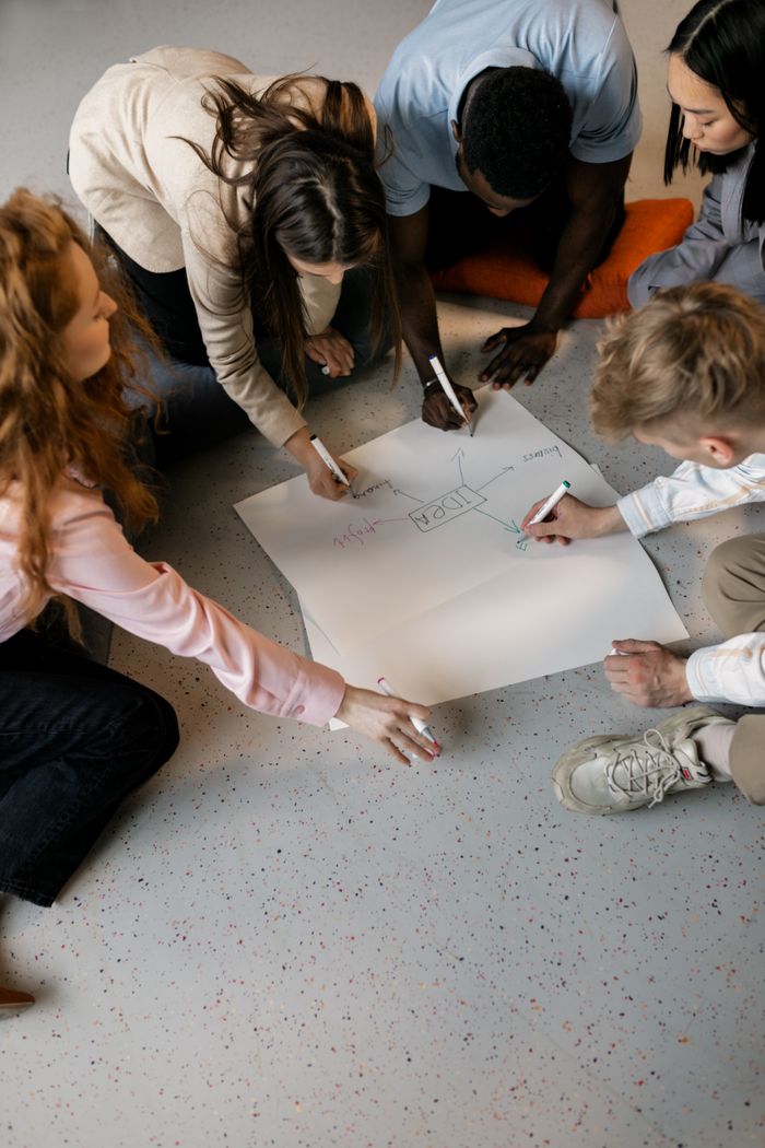 A diverse group of young adults brainstorming and sketching on large sheet paper for strategy planning.