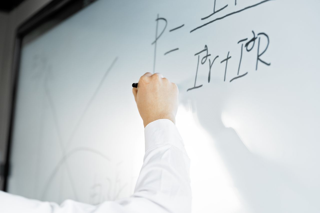 About Close-up of a hand writing a formula on a whiteboard in a professional setting.