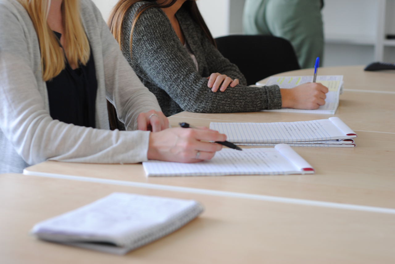 About Group of students writing notes at a meeting in a well-lit classroom.